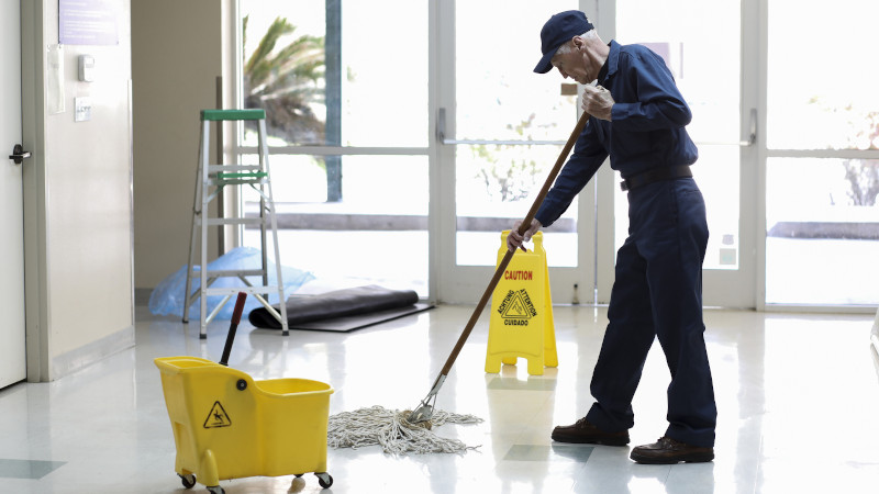 Senior Adult Janitor mops floor at entry to offices.
